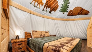 A tent-style room with a bed, wooden nightstand, and a lamp.