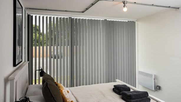 Ein Schlafzimmer mit Bett, Kissen, einer Lampe, einem Heizkörper und einem Fenster mit Jalousien.