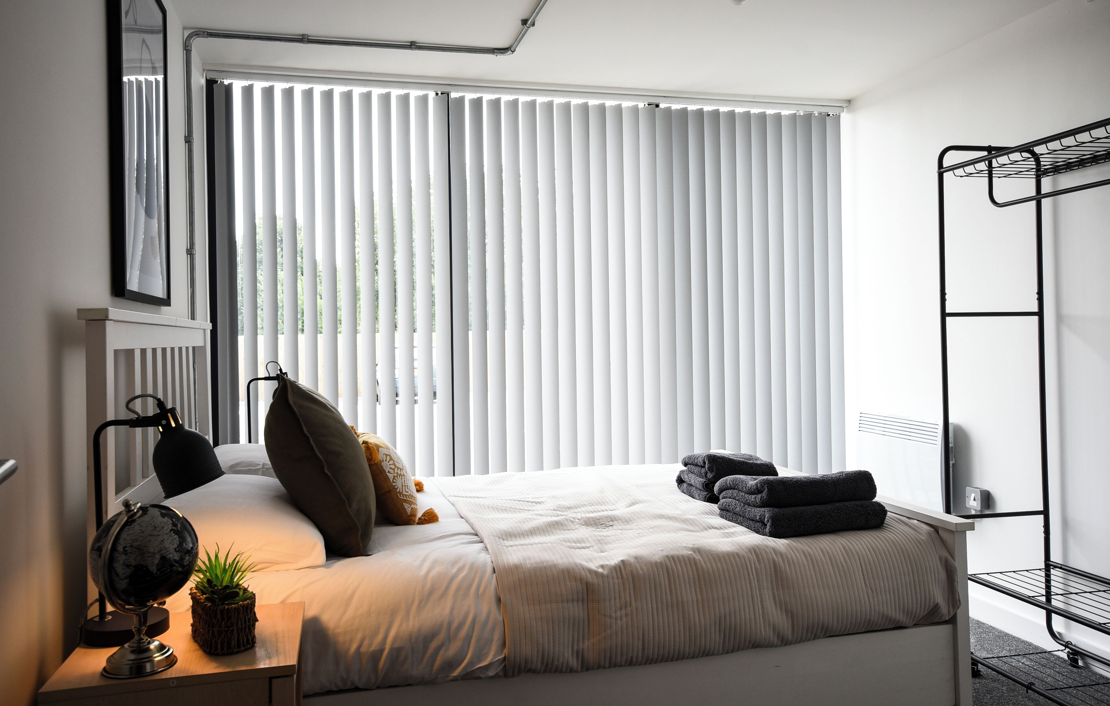 Ein Schlafzimmer mit Bett, Nachttischlampe, Globus, Pflanze und Heizkörper.