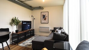 Ein modernes Wohnzimmer mit einer Couch, einem Couchtisch, einem Fernseher, einer Pflanze und einer Heizung.