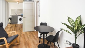 Ein kompakter Wohnbereich mit Essbereich, einer Couch, einem kleinen Tisch und einer Küche mit Waschmaschine.