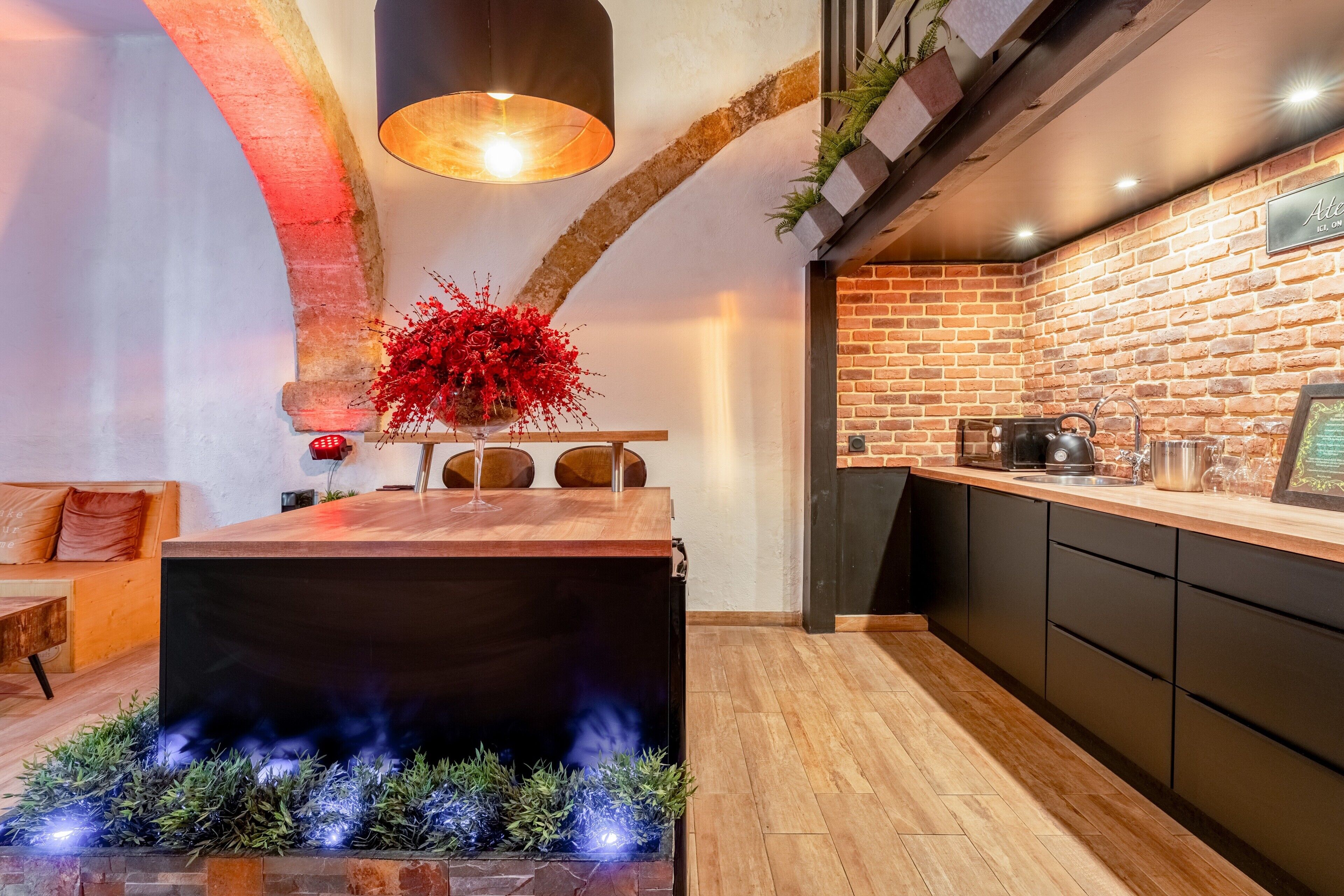 A modern kitchen with a brick wall, wooden countertop, and a central island with a built-in fire feature.