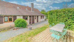 A house with a tiled roof, a chimney, and a gravel driveway. There is a green bush and a table with chairs outside. - Charming farmhouse with swimming pool - calm & nature (Gueugnon)