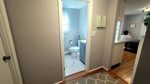 Ein Flur, der zu einem Badezimmer mit Toilette, Waschbecken und Schrank führt.
