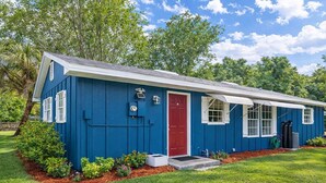 Une maison bleue de plain-pied, avec une porte rouge, des volets blancs et un petit porche.