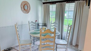 Un coin repas avec une table ronde, quatre chaises, un lustre et une vue sur la verdure environnante.