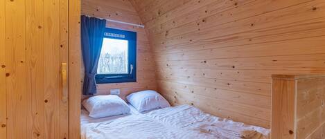 A wooden cabin room with a bed, a window with curtains, and a view of trees.