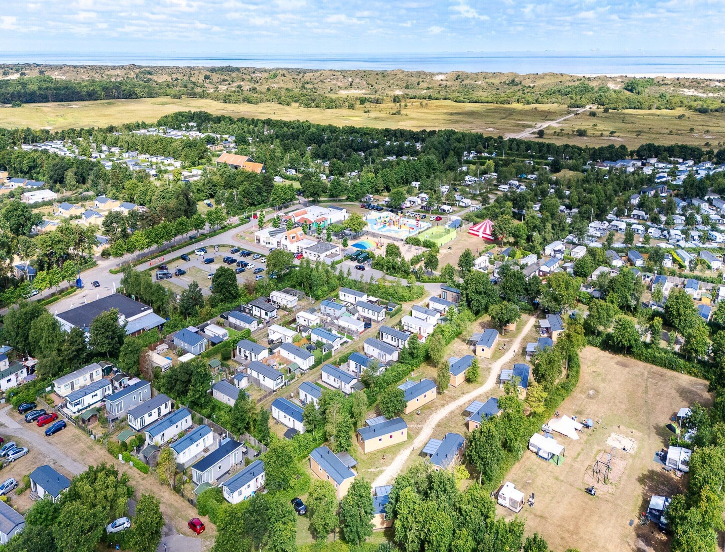 En stor campingplads med flere rækker af mobile hjem, et fællesområde med legeplads og udsigt over det omkringliggende landskab.