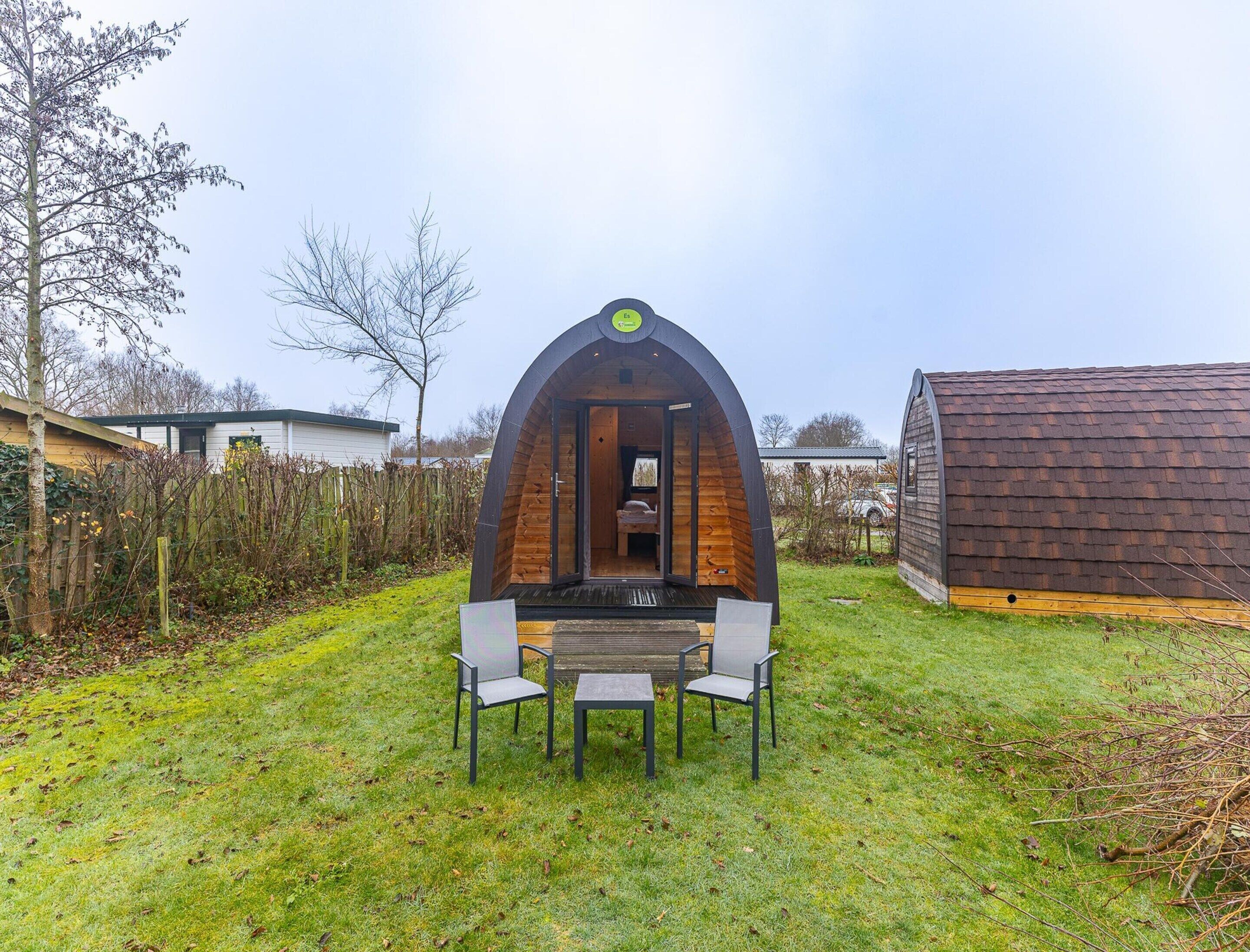 A cozy, semi-open structure with a bench and table in the center, surrounded by a grassy area and a wooden fence.