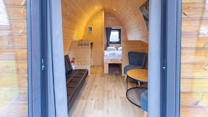 A cozy cabin interior with a wooden ceiling, a bed, a seating area, and a small table. - Zeeland Glamping Lodge for 2 (Burgh-Haamstede)