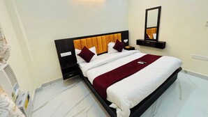 Quarto de hotel moderno com uma cama grande, uma mesinha de cabeceira, um espelho e uma luminária na parede.