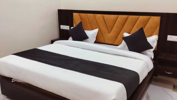 Uma cama com cabeceira de madeira, roupa de cama branca e duas almofadas pretas.