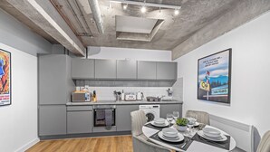 A modern kitchen with grey cabinets, a microwave, and a dining area with a table set for two. - Apartment 18 - The Works (Woolston)