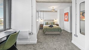 A bedroom with a bed, bedside tables, a desk, a chair, a radiator, and a window with blinds. - Apartment 18 - The Works (Woolston)
