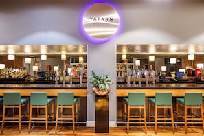 A bar area with a circular sign reading 'TAFARN BAR & KITCHEN,' bar stools, a potted plant, and a well-stocked bar counter. - Majestic Hotel Cardiff (Cardiff)