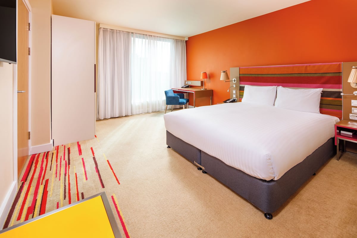 A hotel room with a large bed, a desk, a chair, and a TV.