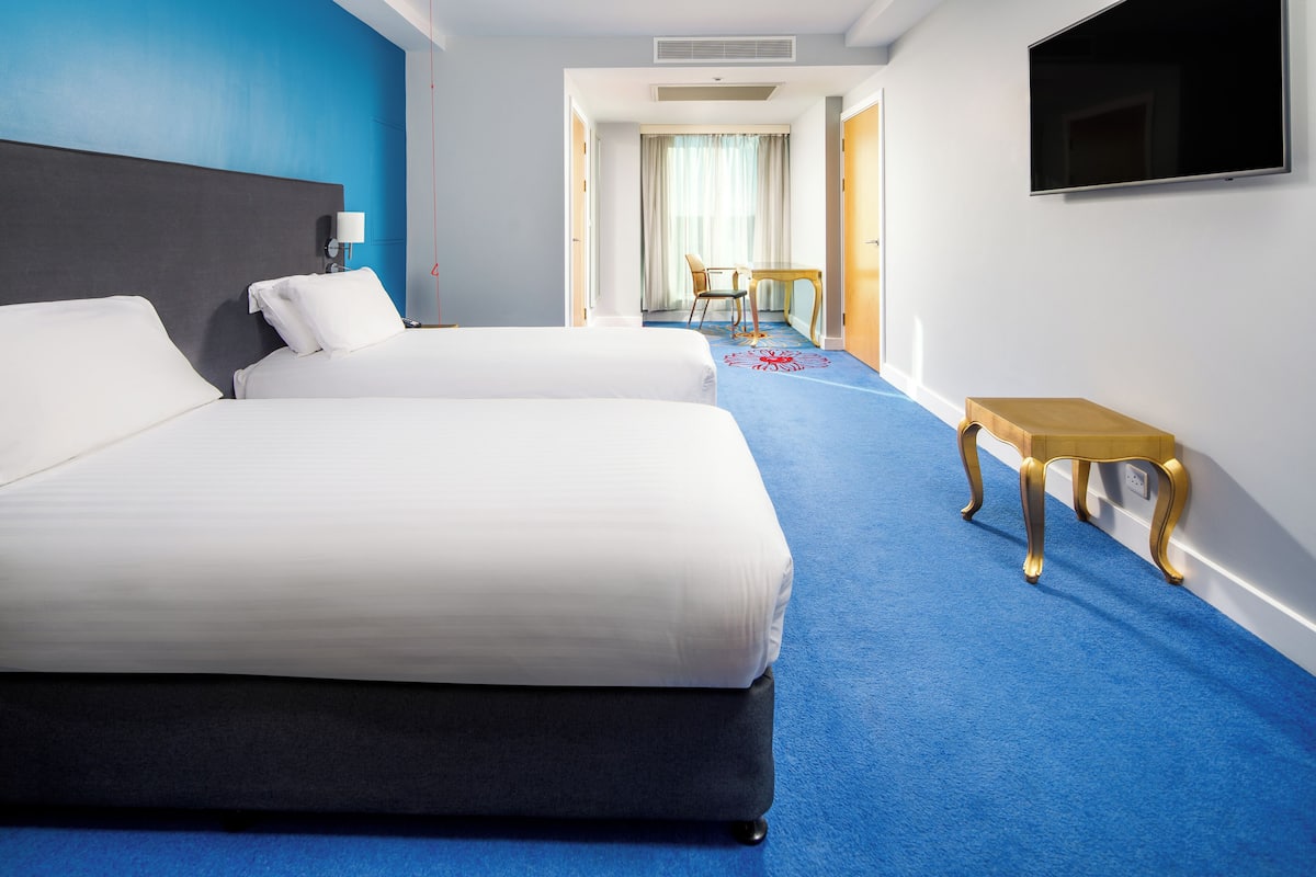 A hotel room with two beds, a TV, a desk, and a chair.