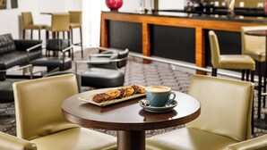 A hotel lobby with leather chairs, a round table with a coffee cup and pastries, and a bar area in the background. - Majestic Hotel Cardiff (Cardiff)