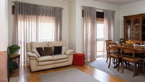 A living room with a beige sofa, a dining table with chairs, and a wooden cabinet.