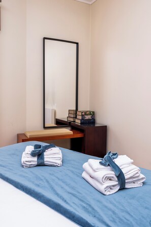 Una habitación de hotel con cama, mesita de noche, espejo y un pequeño escritorio con lámpara.