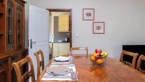 A dining room with a wooden table set for four, chairs, a fruit bowl, and a cabinet with glass doors.