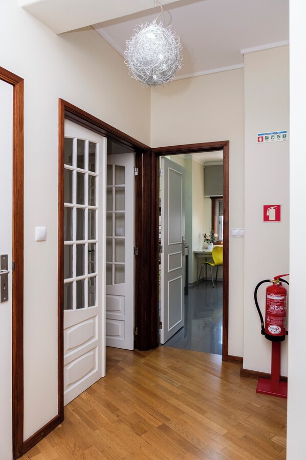 A hallway with wooden flooring, a white door with glass panels, a fire extinguisher, and a ceiling light fixture.