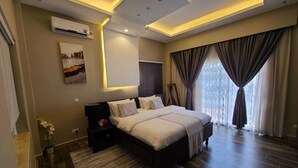 A modern bedroom with a large bed, a bedside table, an air conditioning unit, a wall-mounted TV, and a window with curtains. - BELLEVIEW APARTMENTS NAALYA,KAMPALA,UGANDA (Kampala)