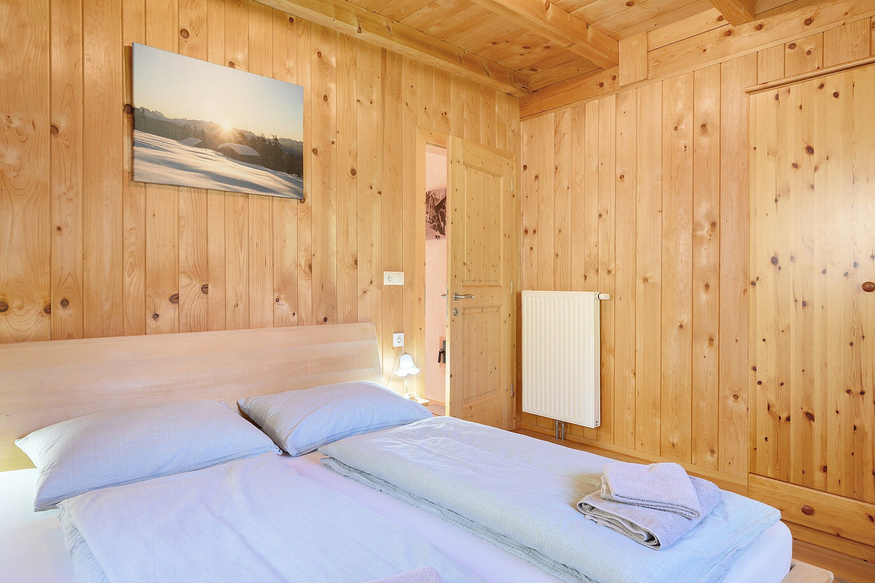 Ein Zimmer mit Holzwänden, einem Bett, einem Gemälde und einer Heizung.
