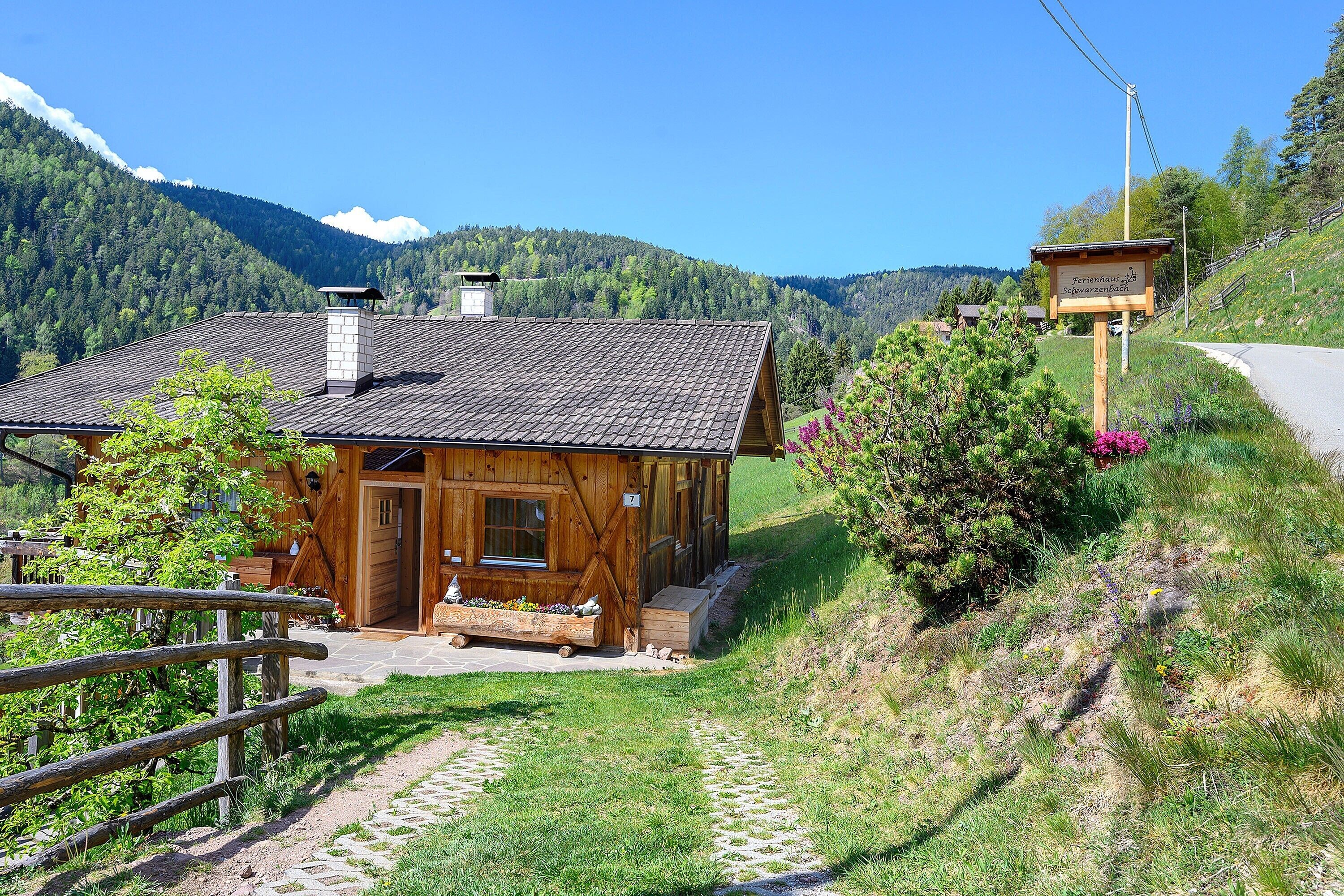 Une cabane en bois avec une cheminée en pierre, une véranda en bois et un sentier en pierre menant à l’entrée.