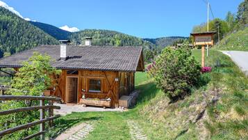 Une cabane en bois avec une cheminée en pierre, une véranda en bois et un sentier en pierre menant à l’entrée.