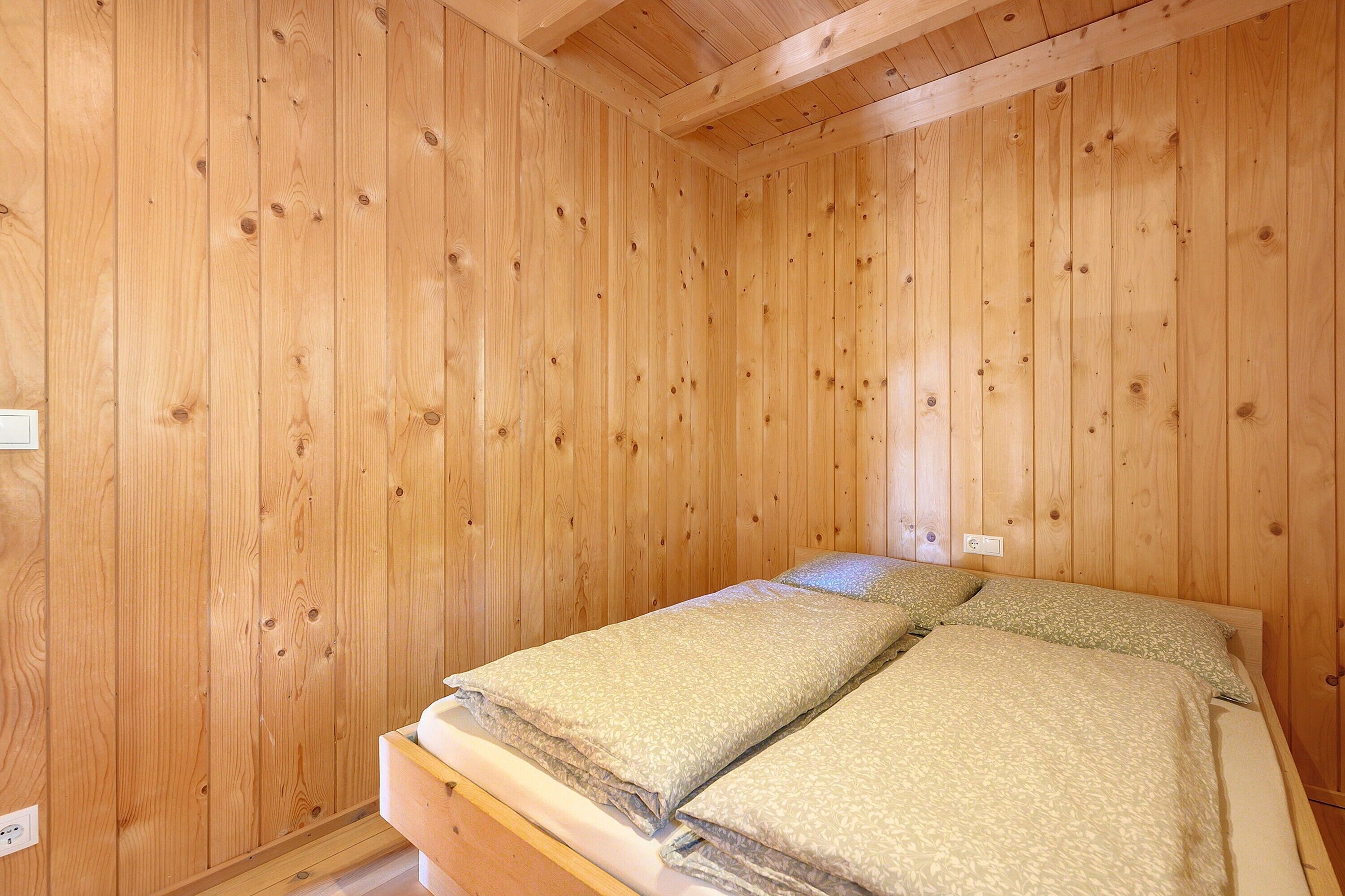 Une pièce aux murs lambrés, avec un lit, une prise de courant et un plafond en bois.