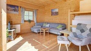 Ein Holzhütten-Innenraum mit einer Couch, einem Sessel, einem kleinen Tisch und einem Fernseher auf einem Schrank.