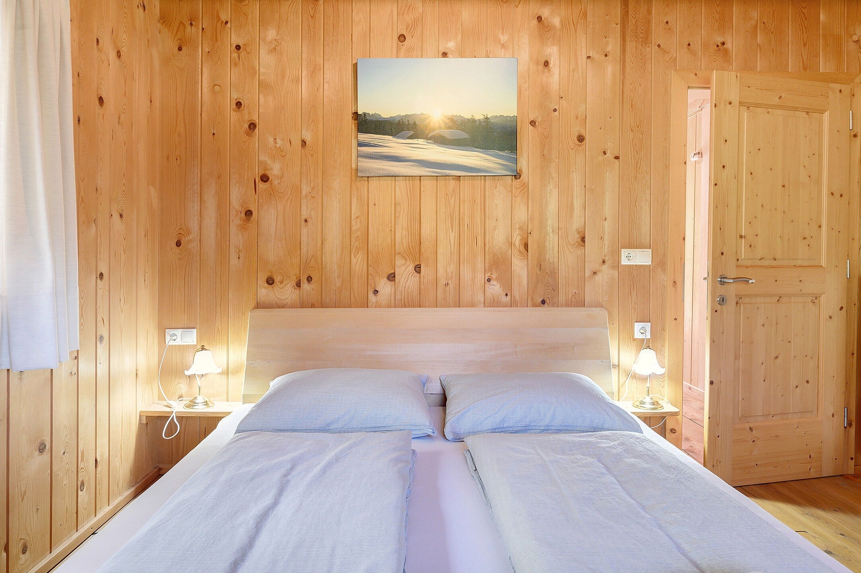 Una habitación con paneles de madera, una cama, dos lámparas de noche y un cuadro en la pared.