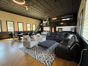 A spacious living room with a large black leather sofa, a white couch, and a dining area with a table and chairs.