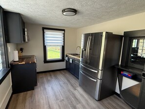A modern kitchen with a stainless steel refrigerator, a built-in oven, and a window with blinds.