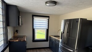 Una cocina compacta con armarios oscuros, un refrigerador de acero inoxidable, una ventana con persianas y una encimera de madera.