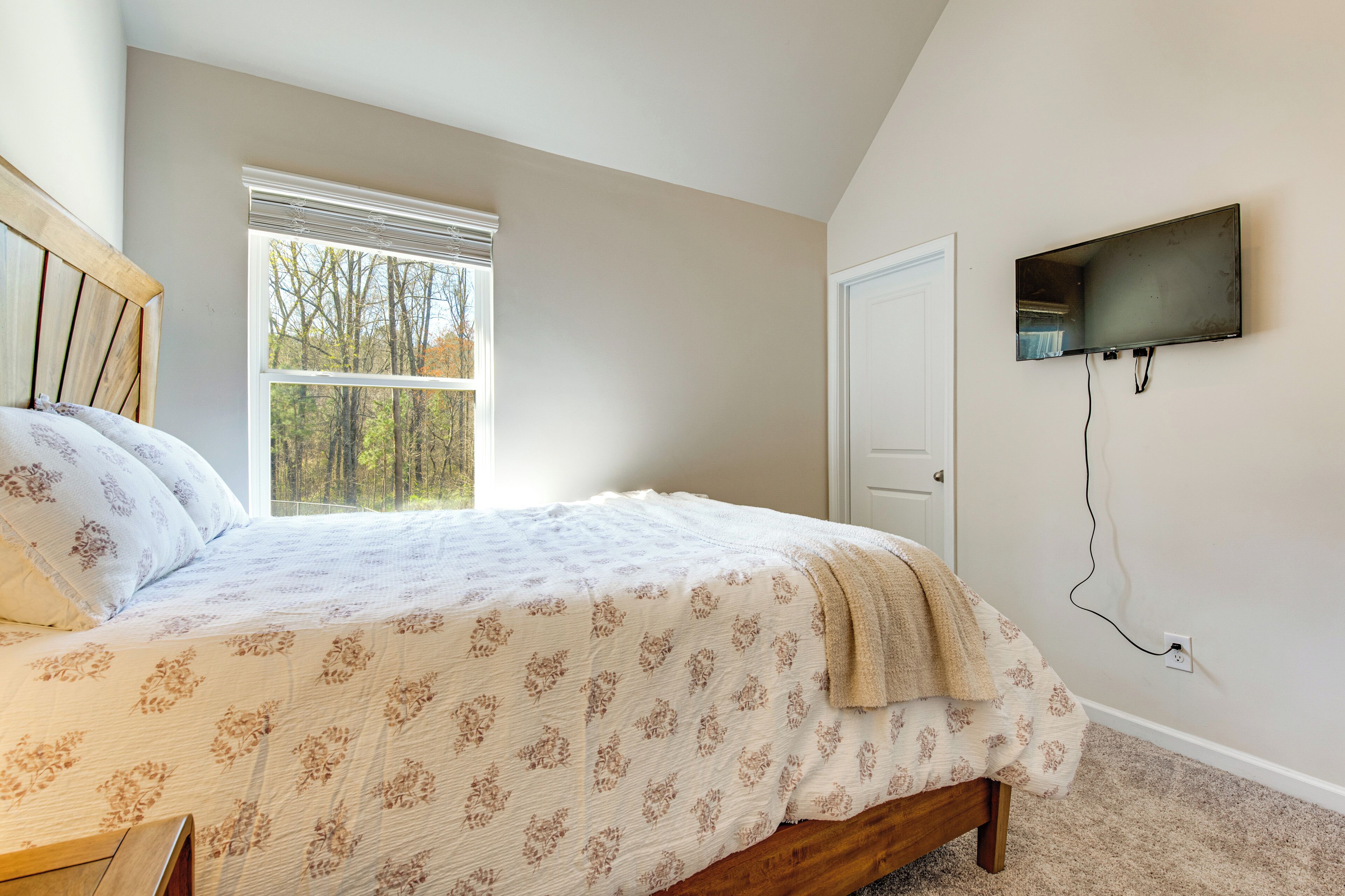 Un dormitorio con cama, ventana, puerta y televisor de pared.