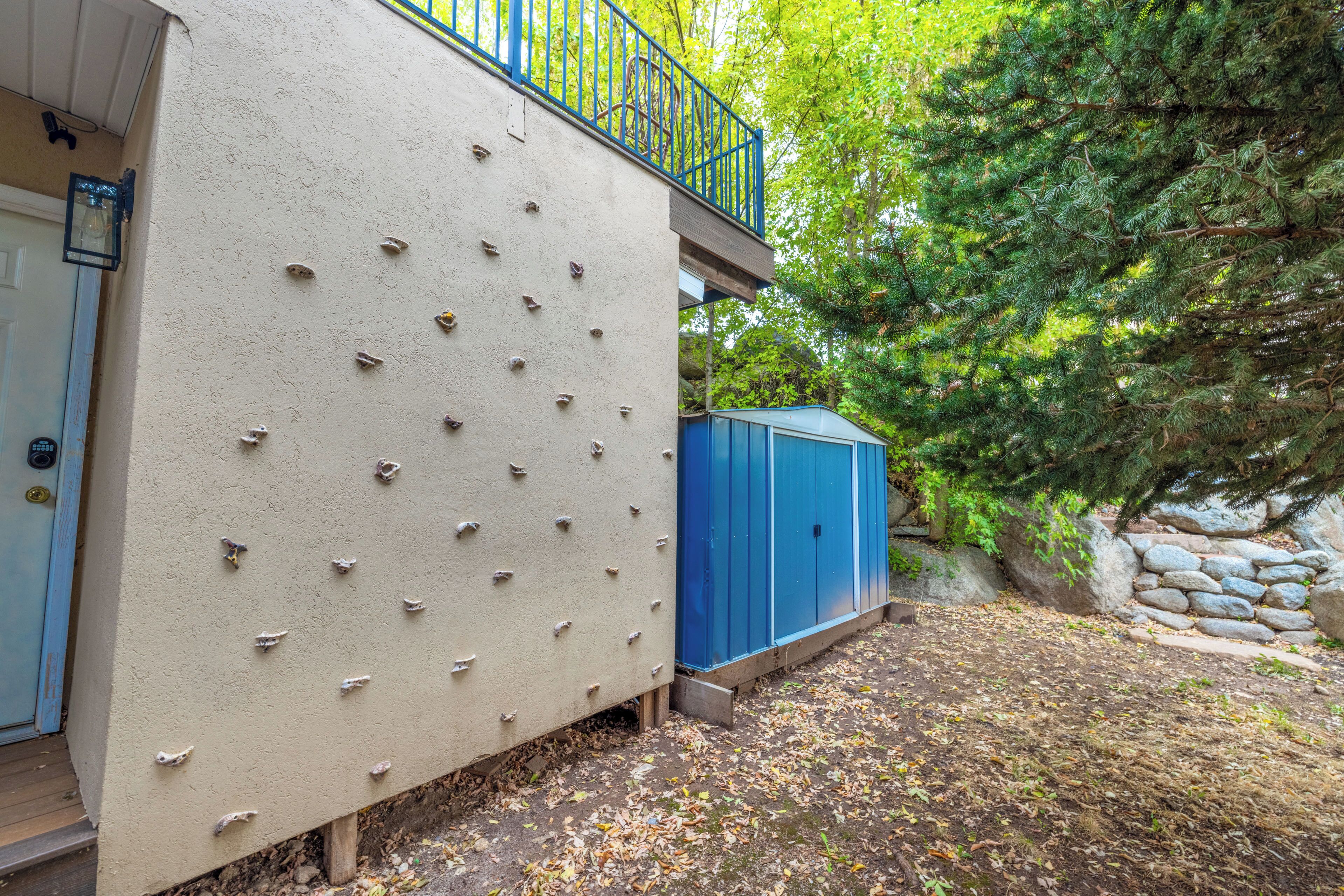 A building with climbing holds on the exterior wall, a blue door, and a blue utility shed.