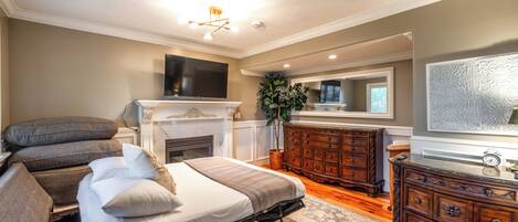 Un dormitorio con cama, sofá, cómoda, televisor y chimenea.