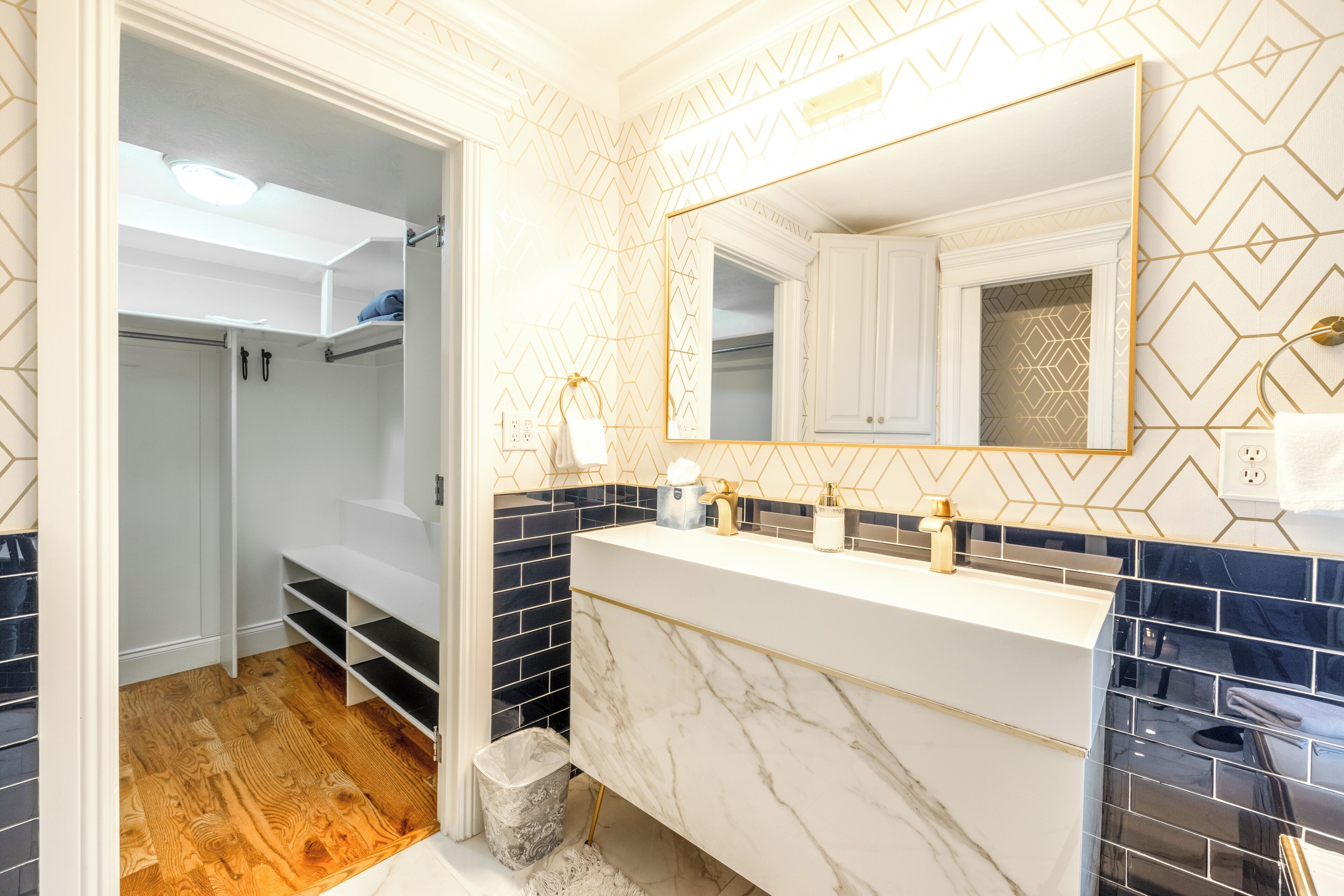 Une salle de bain avec un meuble-lavabo blanc, un grand miroir et un mur orné d’un motif géométrique.