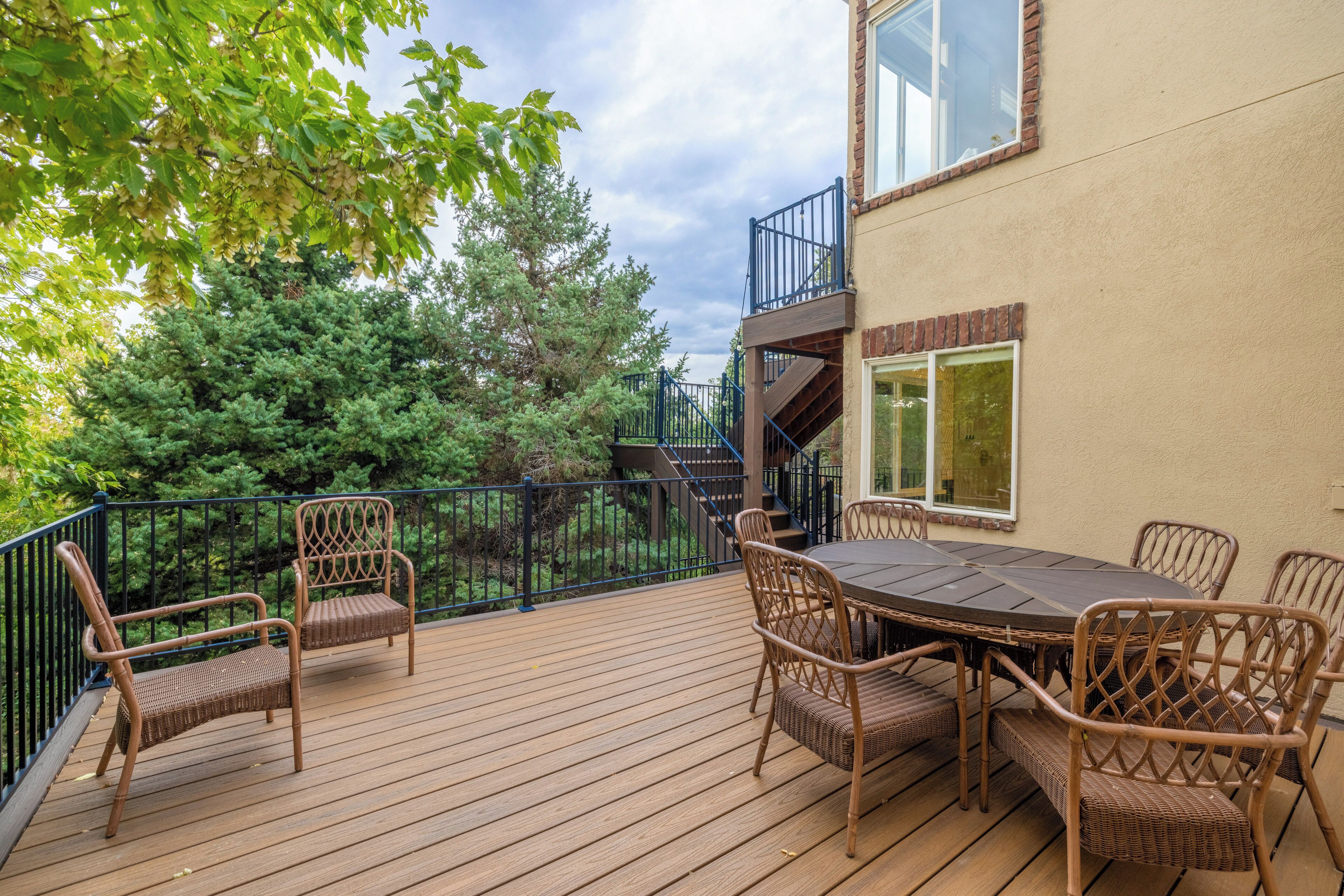 Une terrasse en bois avec des meubles en osier, un escalier et une vue sur les arbres.