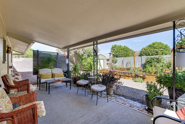 A covered patio area with wicker furniture, potted plants, and a view of the backyard.