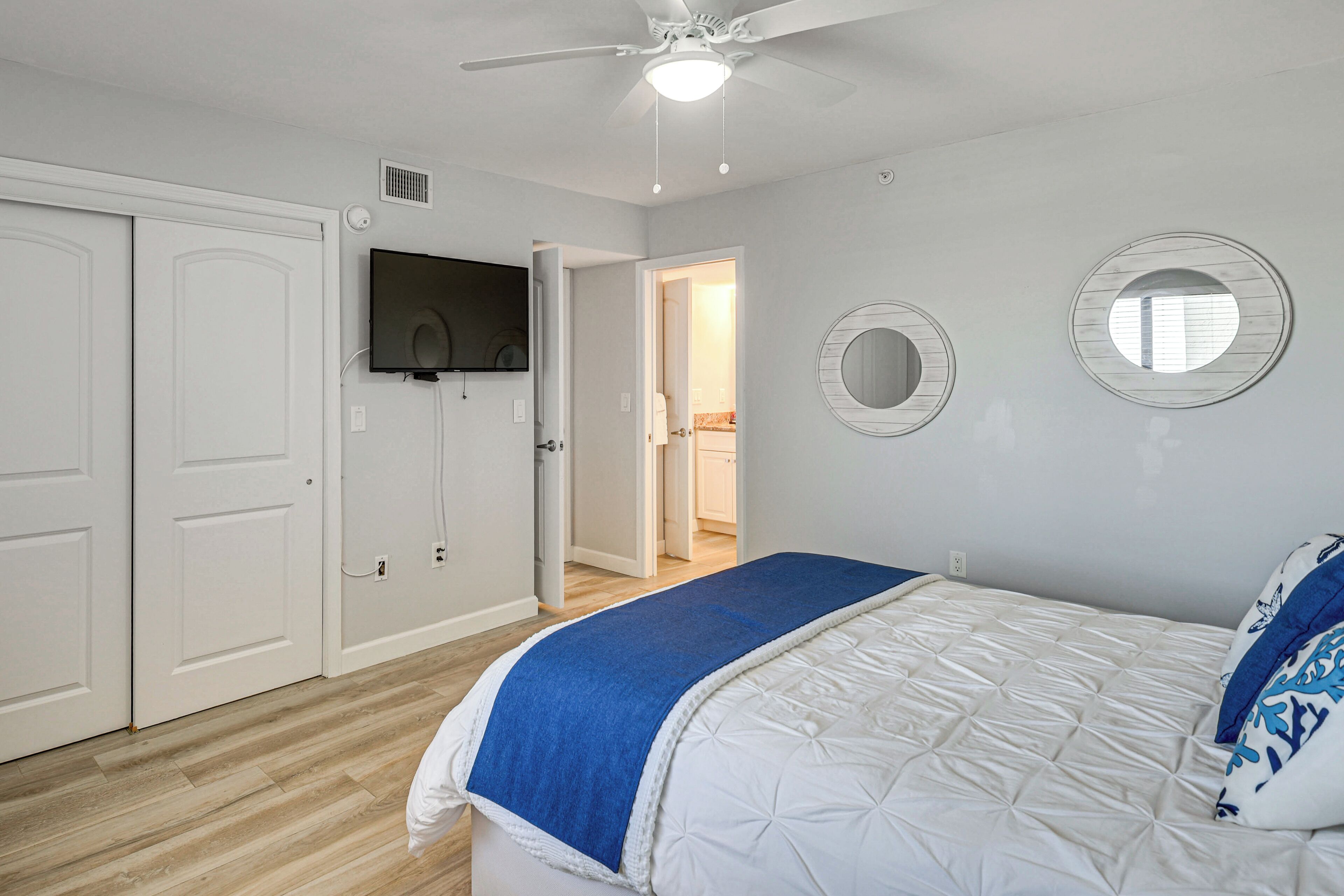 A bedroom with a bed, a ceiling fan, a TV, and a door leading to another room.