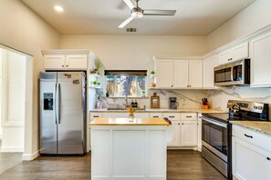 A kitchen with white cabinetry, a stainless steel refrigerator, a microwave, an oven, and a wooden island. - Ultimate Stockyards Base! Home w/ Bonus Apartment (Fort Worth)