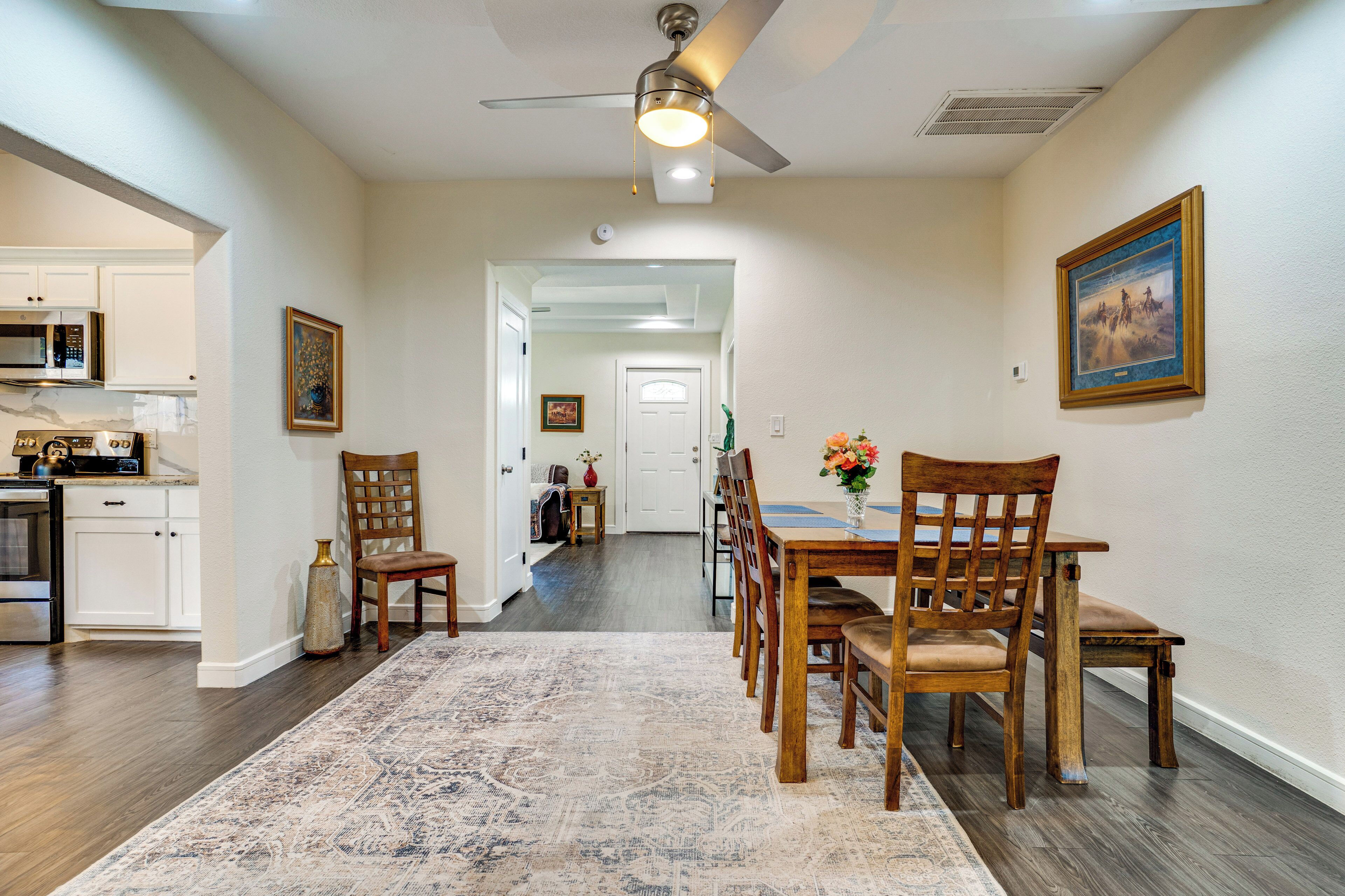 A dining area with a table and chairs, a ceiling fan, and a kitchen in the background.