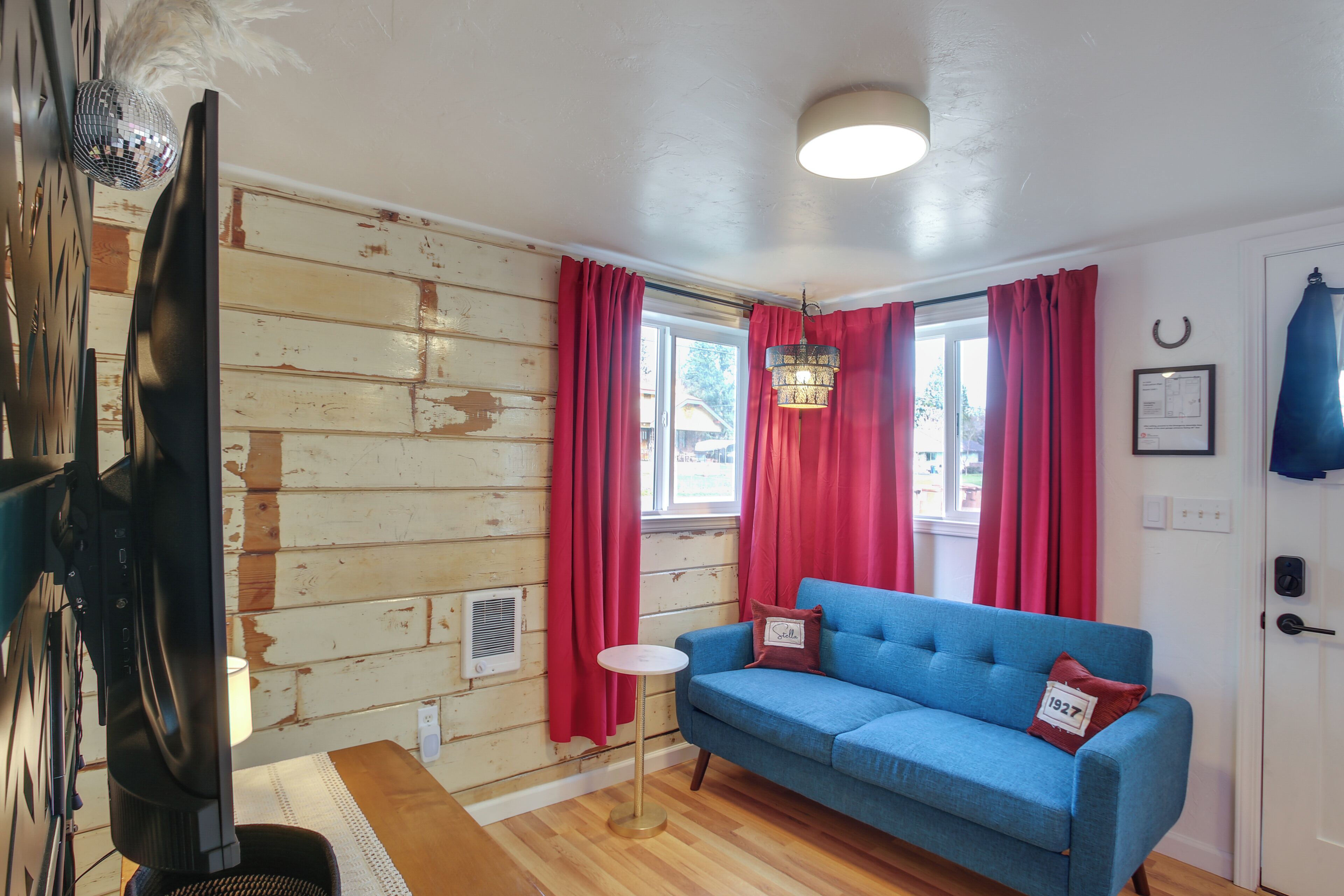 A room with a blue sofa, red curtains, a small table, a television, and a wooden wall.