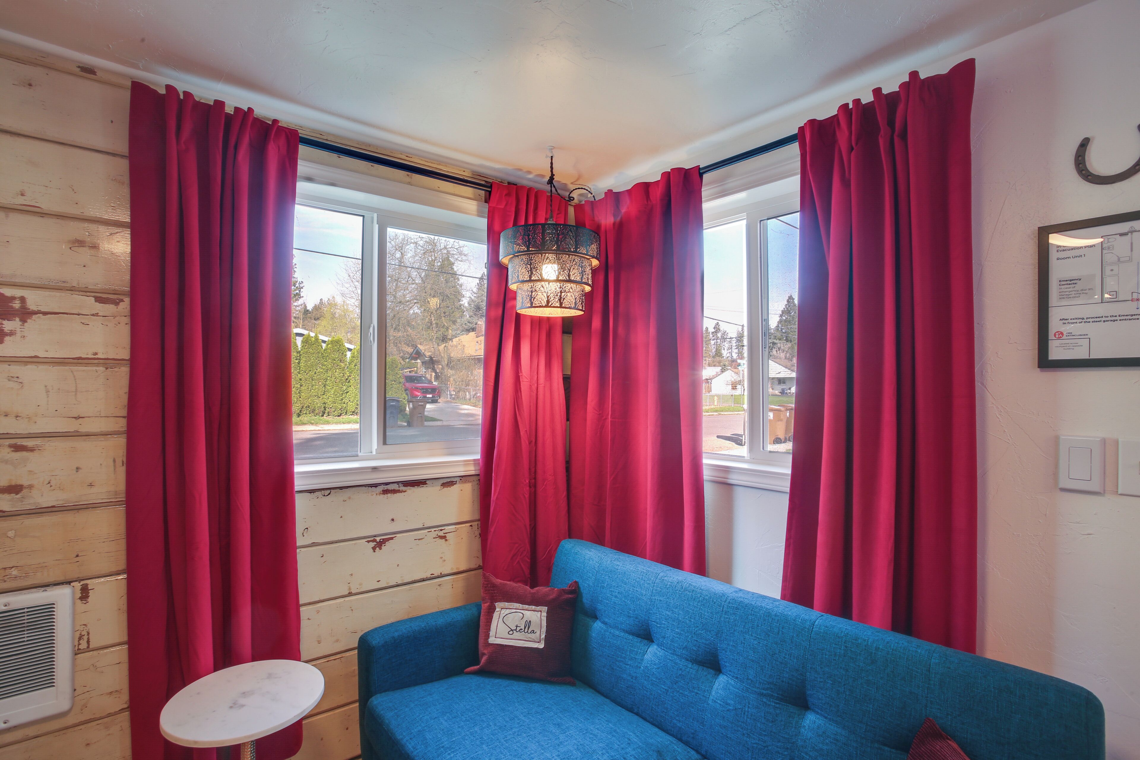 A room with a blue sofa, red curtains, a hanging light fixture, and a small table.