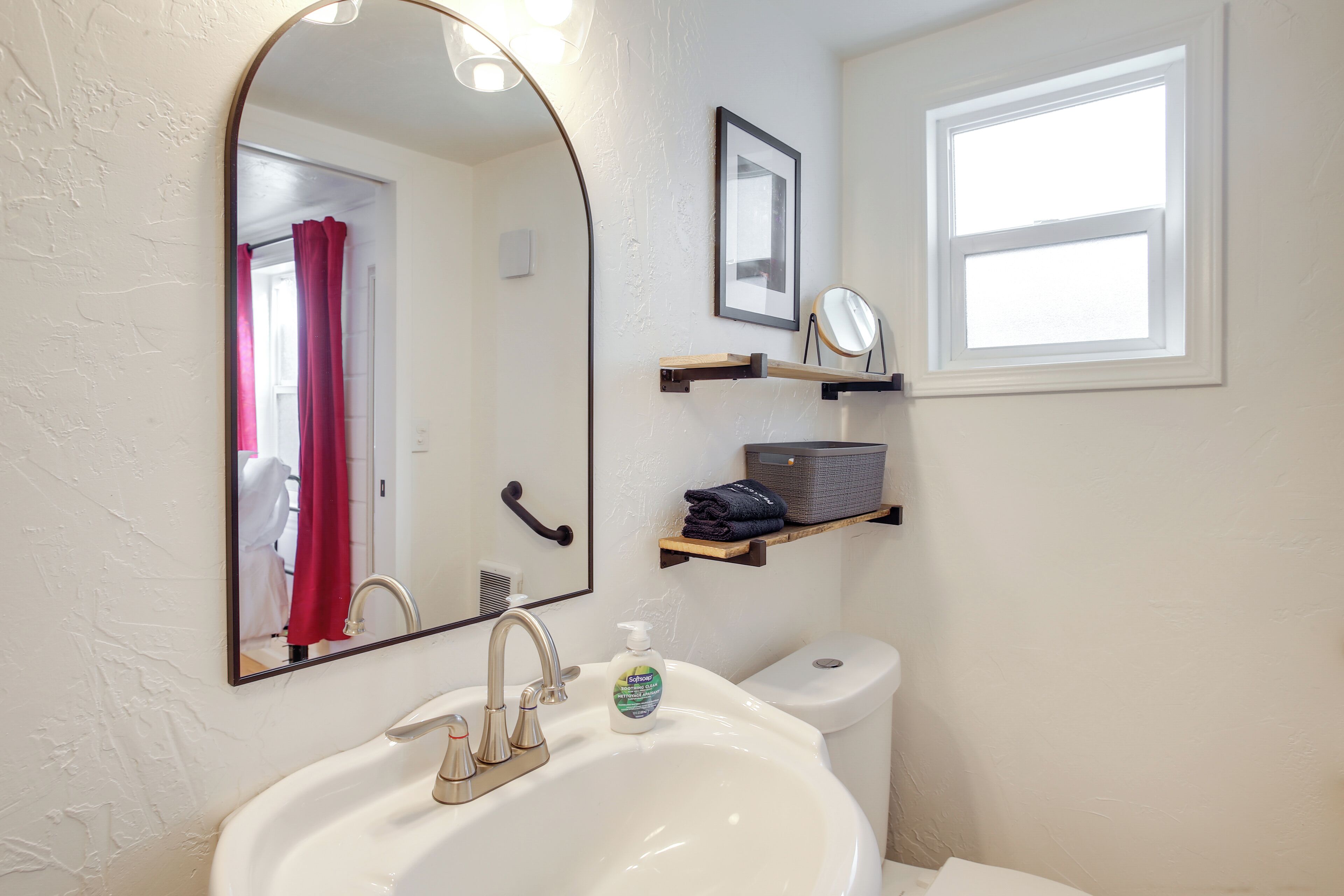 Une salle de bain avec un lavabo blanc, un miroir, une fenêtre et des toilettes.
