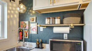 Una cocina moderna con un lavamanos de acero inoxidable, un microondas y una estantería con frascos y una cesta.
