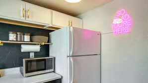 Una cocina con un refrigerador blanco, un microondas y un letrero de neón en la pared.